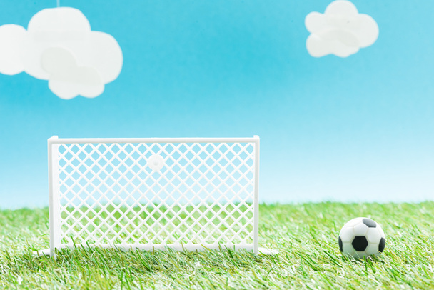 игрушечные футбольные ворота и мяч на зеленой траве на синем фоне с облаками, концепция ставок на спорт
 - Фото, изображение
