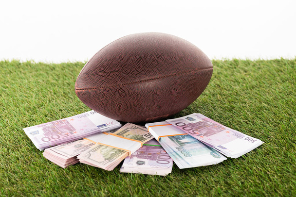 rugby ball near packs of euro and dollar banknotes on green grass isolated on white, sports betting concept - Fotoğraf, Görsel