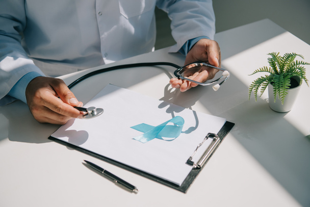 partial view of doctor holding stethoscope near blue awareness ribbon on clipboard with blank paper - Φωτογραφία, εικόνα