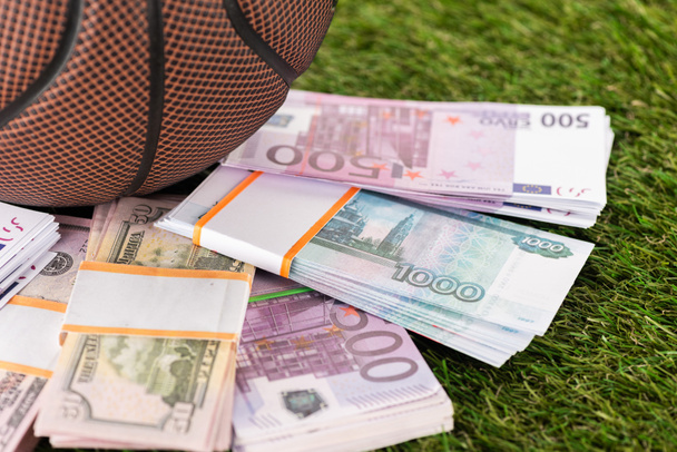 close up view of baseball ball near dollar and euro banknotes on green grass, sports betting concept - Foto, afbeelding