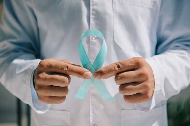 partial view of doctor in white coat holding blue awareness ribbon  - Foto, immagini