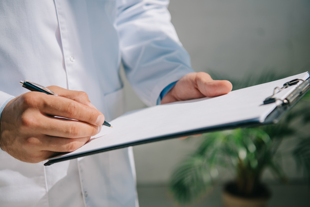 cropped view of doctor in white coat writing diagnosis on clipboard  - Foto, Imagen