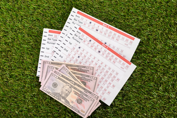 top view of dollar banknotes and betting lists on green grass, sports betting concept - Foto, Bild