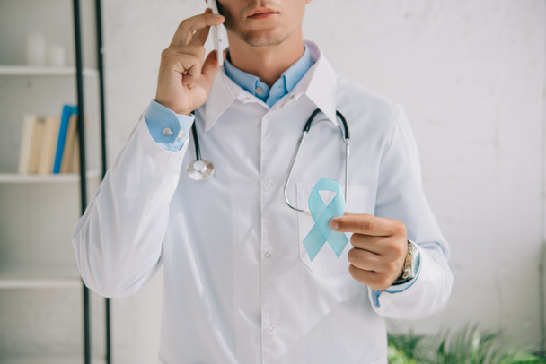 przycięty widok lekarza trzymającego niebieską wstążkę świadomości podczas rozmowy na smartfonie - Zdjęcie, obraz