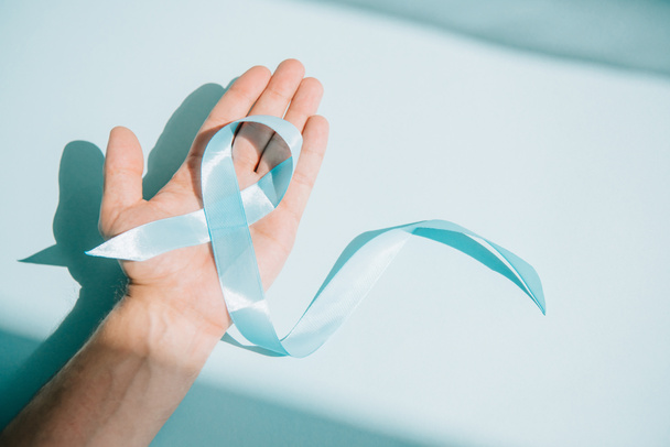 partial view of male hand with blue awareness ribbon on white background - Fotó, kép