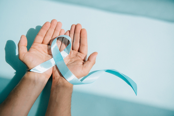 cropped view of male hands with blue awareness ribbon on white background - Фото, зображення