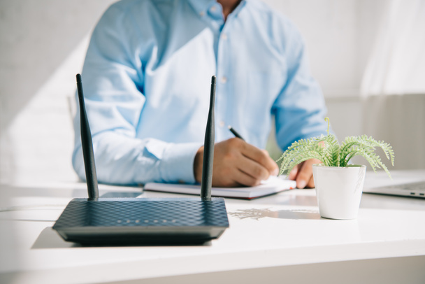 cropped view of businessman writing in notebook near router and flowerpot - Photo, Image