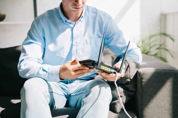 przycięty widok biznesmena siedzącego na kanapie i trzymającego podłączony router - Zdjęcie, obraz