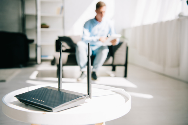selective focus of black plugged router on white table and businessman sitting on sofa - Photo, Image