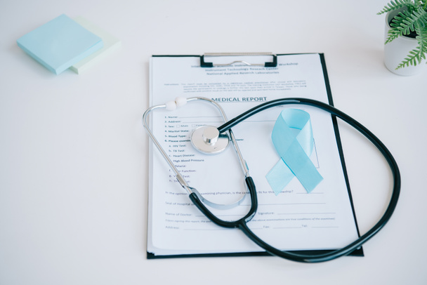 modrá informační stuha, lékařská zpráva, stetoskop a lepicí poznámky na bílém stole - Fotografie, Obrázek