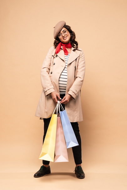 pregnant french woman in coat holding shopping bags on beige background  - Photo, Image