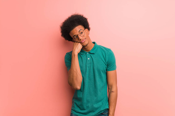 junger afrikanisch-amerikanischer Mann über einer rosafarbenen Wand, der an etwas denkt und zur Seite schaut - Foto, Bild