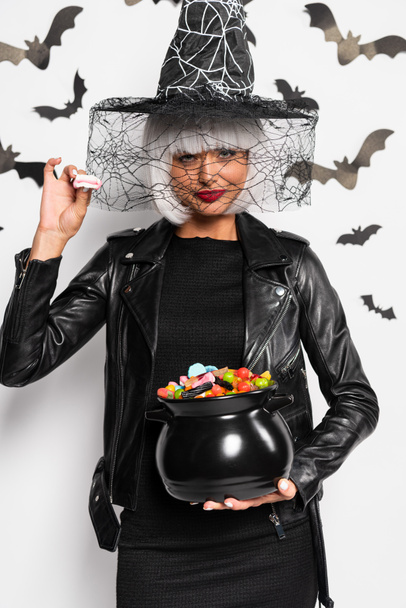 attractive woman in witch hat and wig holding pot with candies in Halloween - Foto, immagini
