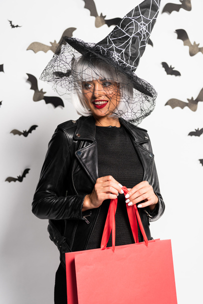 smiling woman in witch hat and wig holding shopping bag in Halloween - Фото, зображення