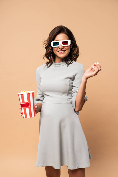 pregnant woman in grey dress with 3d glasses touching belly and holding popcorn on beige background  - Foto, Imagen