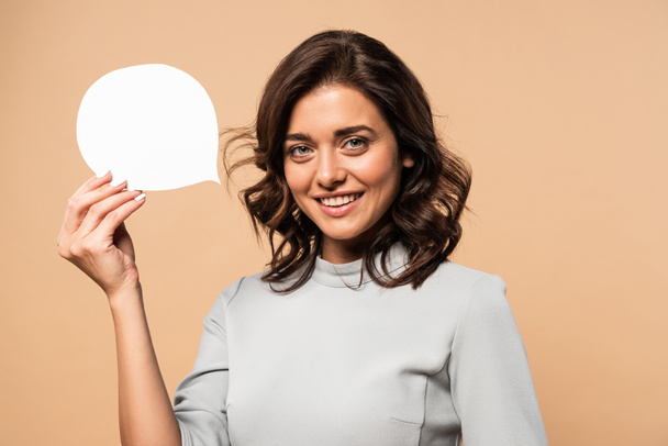 smiling woman in grey dress holding speech bubble isolated on beige  - Foto, Imagem