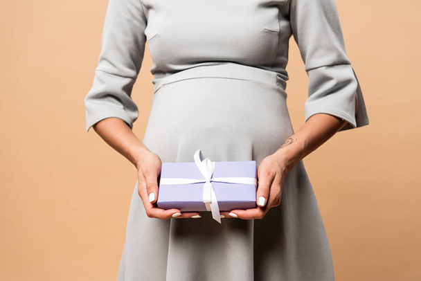 cropped view of pregnant woman in grey dress holding gift on beige background - Foto, immagini
