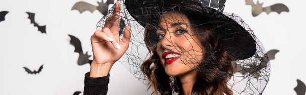 panoramic shot of attractive woman in witch hat looking at camera in Halloween - Foto, afbeelding