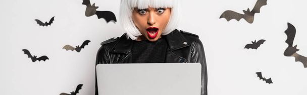 panoramic shot of shocked woman in wig looking at laptop in Halloween - Photo, Image