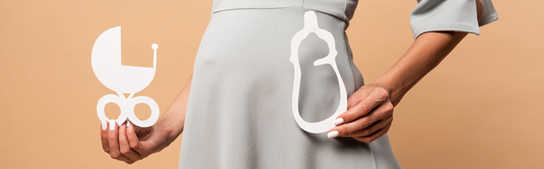 πανοραμική λήψη της εγκύου σε γκρι φόρεμα κρατώντας χαρτί μεταφοράς μωρό και μπουκάλι σε μπεζ φόντο  - Φωτογραφία, εικόνα