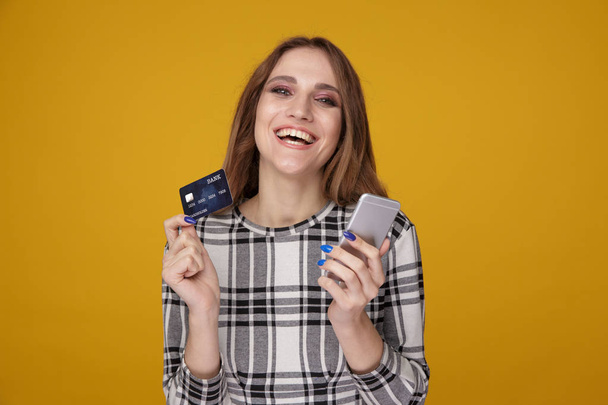 Όμορφη γυναίκα που δείχνει την πιστωτική κάρτα και χρησιμοποιώντας το κινητό που στέκεται απομονωμένη. - Φωτογραφία, εικόνα