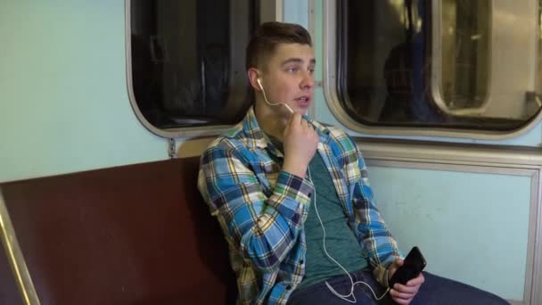 A young man speaks on the phone through headphones in a subway train. Old subway car - Felvétel, videó