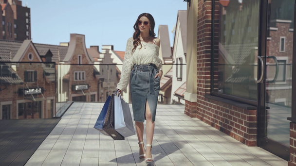 Güneş gözlüklü bir kadın alışveriş torbalarıyla yürüyor.  - Video, Çekim