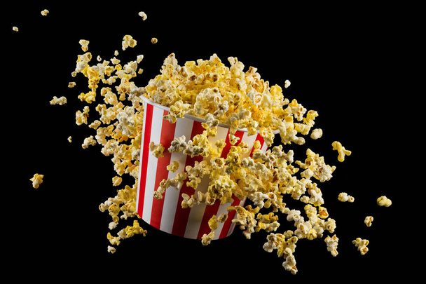 Flying popcorn from striped bucket isolated on black background - Fotografie, Obrázek