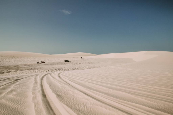 Paysage d'un désert avec des traces de pneus sur le sable et des véhicules à moteur au loin
 - Photo, image