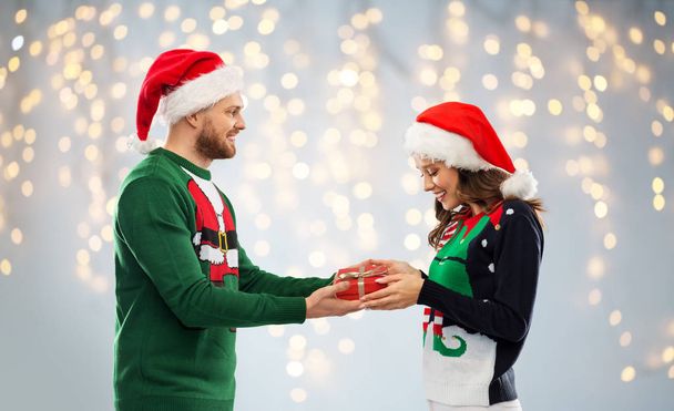 happy couple in ugly sweaters with christmas gift - Photo, Image