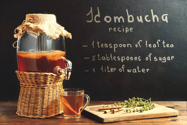 Fresh homemade kombucha fermented tea drink in a jar with faucet and in a cup and recipe on a dark wall - Valokuva, kuva