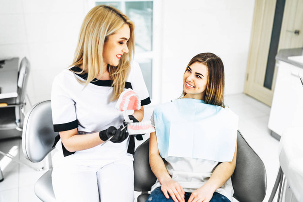 Pretty female dentist explaining way of treatment on the denture - Foto, imagen