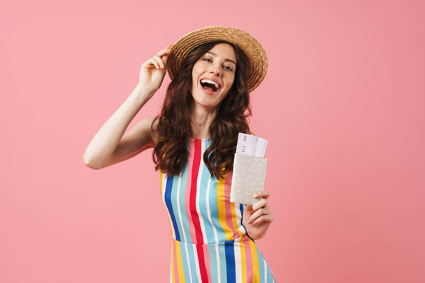 Positive happy young cute woman posing isolated over pink wall background holding passport with tickets. - Фото, изображение