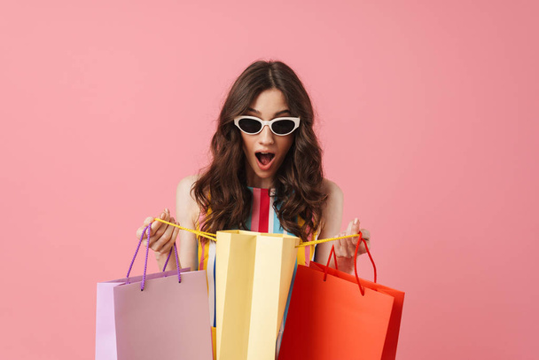 Beautiful pleased positive happy young cute woman posing isolated over pink wall background holding shopping bags. - Fotó, kép