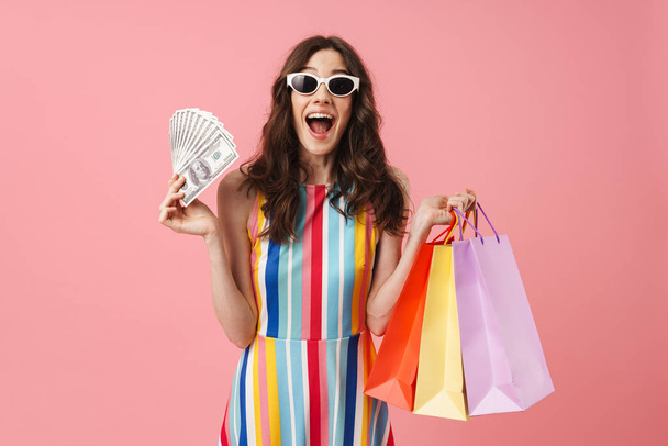 Beautiful pleased positive happy young cute woman posing isolated over pink wall background holding shopping bags. - Φωτογραφία, εικόνα