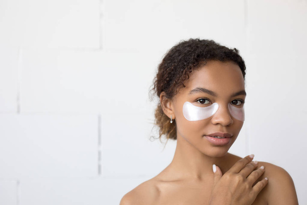 Young afro american woman with collagen pads under her eyes on white background. - Valokuva, kuva