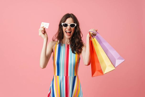 Beautiful pleased positive happy young cute woman posing isolated over pink wall background holding shopping bags. - Foto, Imagen