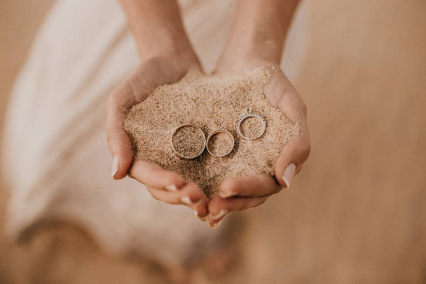 Closeup shot of female hands holding sand with three rings on the top - Fotoğraf, Görsel