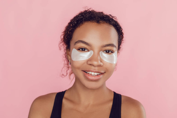 Young afro american woman with collagen pads under her eyes on pink background. - Foto, Bild