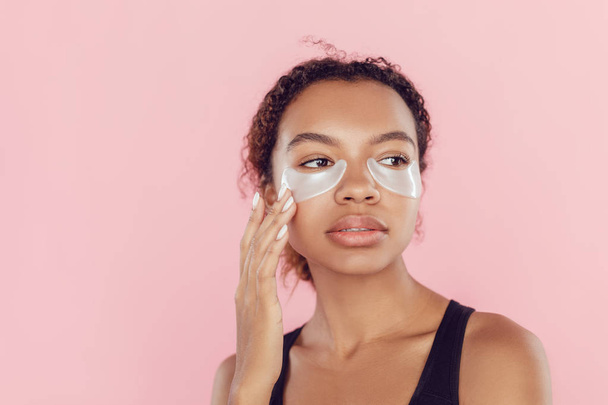 Young afro american woman with collagen pads under her eyes on pink background. - Φωτογραφία, εικόνα
