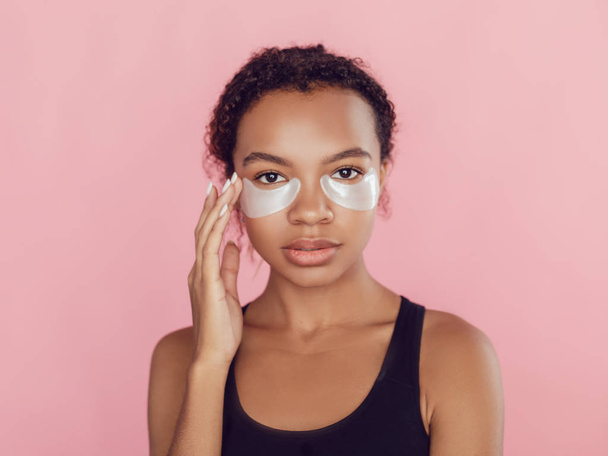 Young afro american woman with collagen pads under her eyes on pink background. - Zdjęcie, obraz