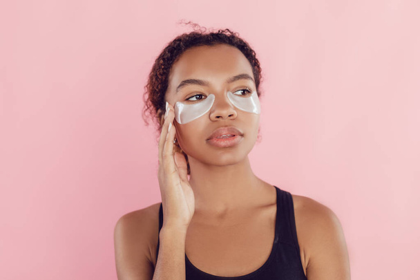 Young afro american woman with collagen pads under her eyes on pink background. - Foto, imagen