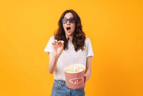 Scared shocked young woman posing isolated over yellow wall background eat popcorn watch film. - Foto, Imagem