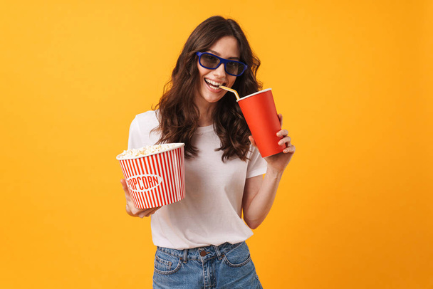 Happy cheerful smiling young woman posing isolated over yellow wall background eat popcorn watch film. - Photo, Image