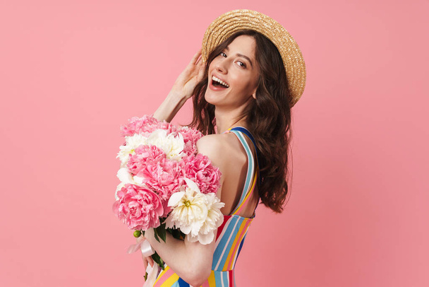 Happy cheery smiling young cute woman posing isolated over pink wall background holding flowers. - Фото, изображение