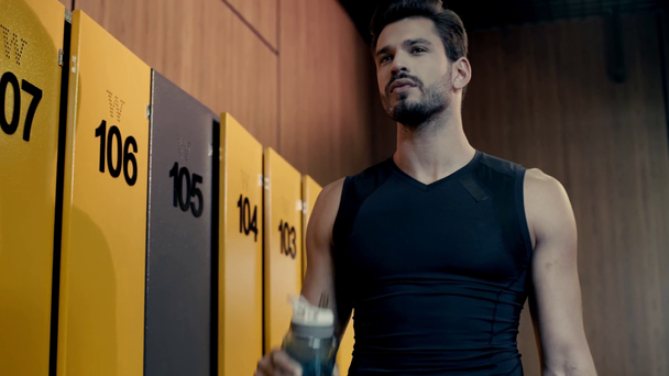 handsome sportsman drinking water in locker room  - Footage, Video