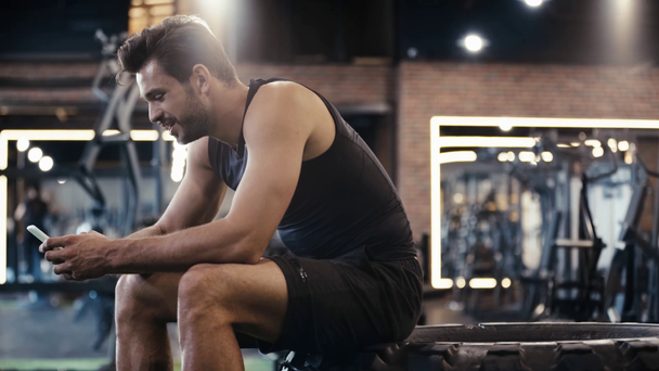szczęśliwy sportowiec za pomocą smartfona w siłowni - Materiał filmowy, wideo
