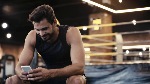 wesoły sportowiec za pomocą smartfona w siłowni - Materiał filmowy, wideo