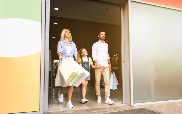 Familia dejando Hypermarket llevando coloridas bolsas de compras
 - Foto, imagen