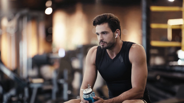 bearded sportsman listening music and drinking water in gym  - Footage, Video